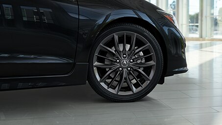 Low, angled shot of the front side of a black Acura parked inside a showroom during the day. // Plan bas et incliné de l’avant d’une Acura noire garée dans une salle d’exposition pendant la journée.