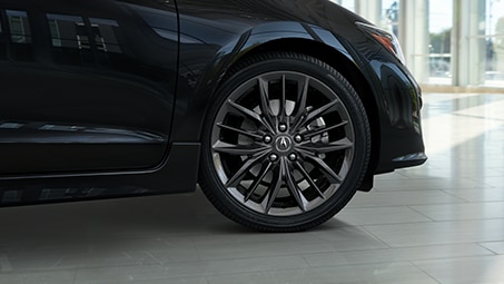 Low, angled shot of the front side of a black Acura parked inside a showroom during the day. // Plan bas et incliné de l’avant d’une Acura noire garée dans une salle d’exposition pendant la journée.