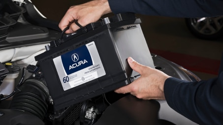 Close-up shot of a technician reaching into the open hood of an Acura to install a battery.  	Gros plan d’un technicien qui pénètre dans le capot ouvert d’une Acura pour installer une batterie.