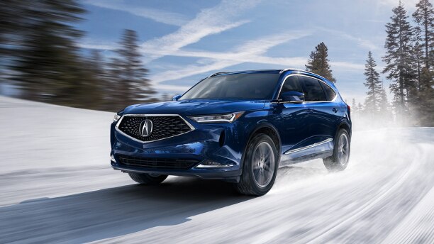 An MDX driving through the hills during the winter over a road that is covered in snow. // Un MDX roulant à travers les collines pendant l'hiver sur une route couverte de neige.