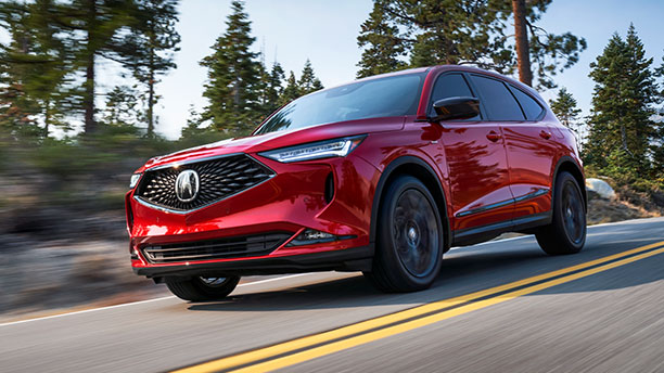 Side-angle, front end view of a steel metallic, all-new 2022 Acura MDX driving through a desert. 