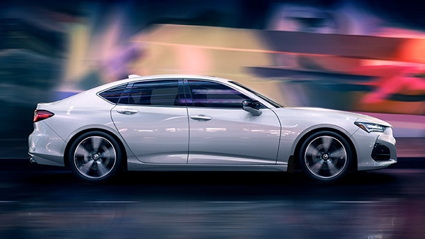 Side profile shot of a white Honda driving through the night with the background blurred in a flurry of vibrant colours./Photo de profil d'une Honda blanche roulant dans la nuit, l'arrière-plan étant flou dans une rafale de couleurs vives.